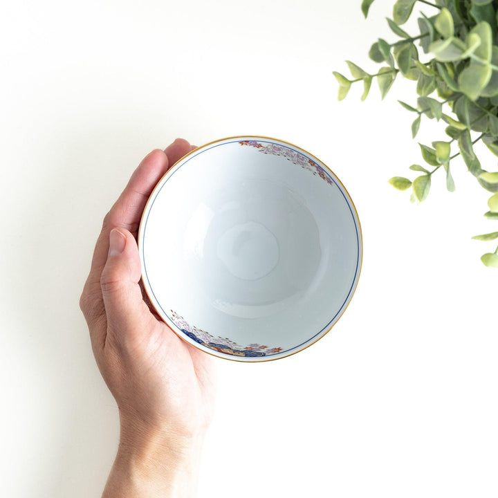 A round ceramic rice bowl with detailed traditional Japanese designs of trees and clouds in blue, red, and green on a white background.