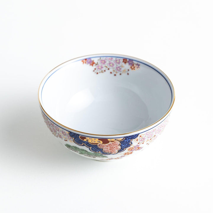 A round ceramic rice bowl with detailed traditional Japanese designs of trees and clouds in blue, red, and green on a white background.
