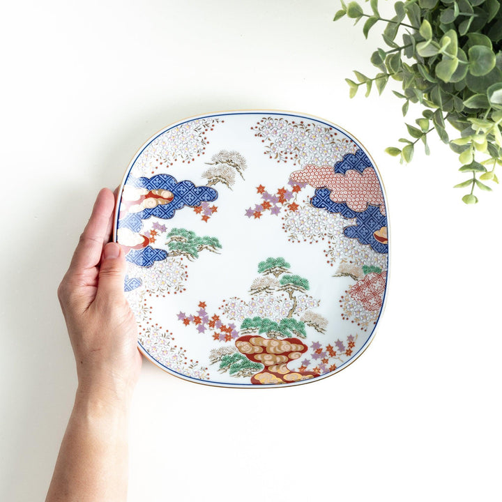 A square salad plate featuring a traditional Japanese landscape with trees, clouds, and maple leaves, framed by intricate blue and red patterns.