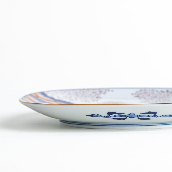 A square salad plate featuring a traditional Japanese landscape with trees, clouds, and maple leaves, framed by intricate blue and red patterns.