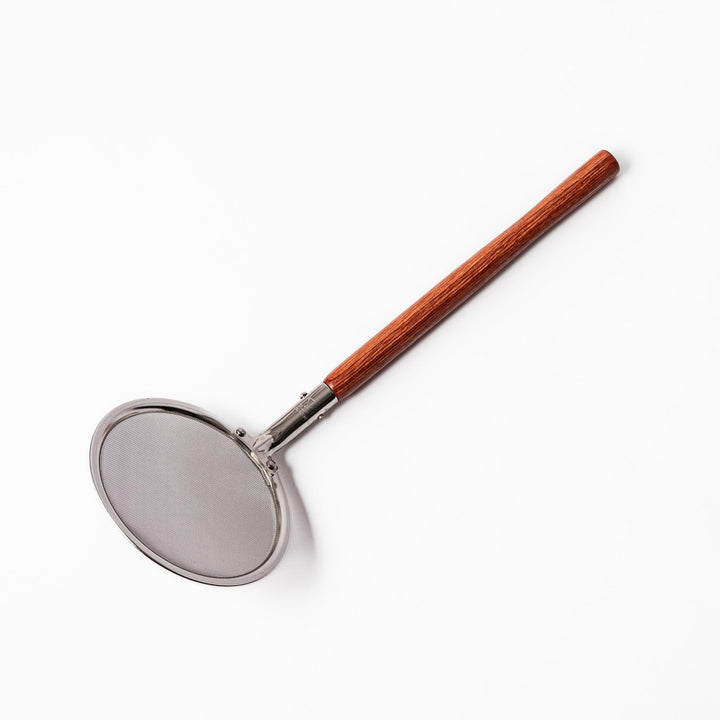 Stainless steel round-mesh skimmer with long wooden handle, perfect for straining soups and frying in home kitchens.