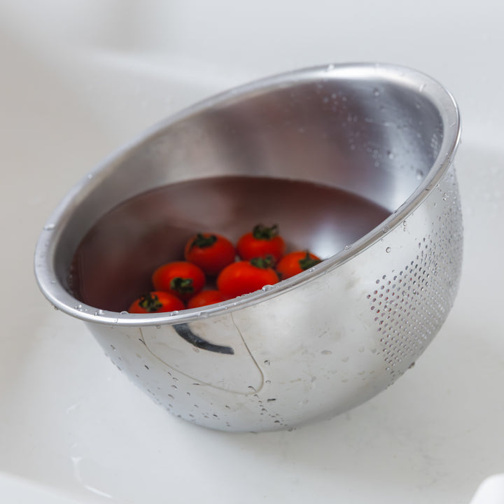 Cherry tomatoes soaking in water inside a stainless steel colander, ready to be washed in the kitchen sink.