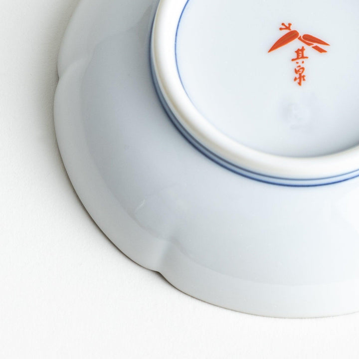 A round white sauce dish with delicate floral and ribbon patterns in gold, green, and red, accented by small scalloped edges.