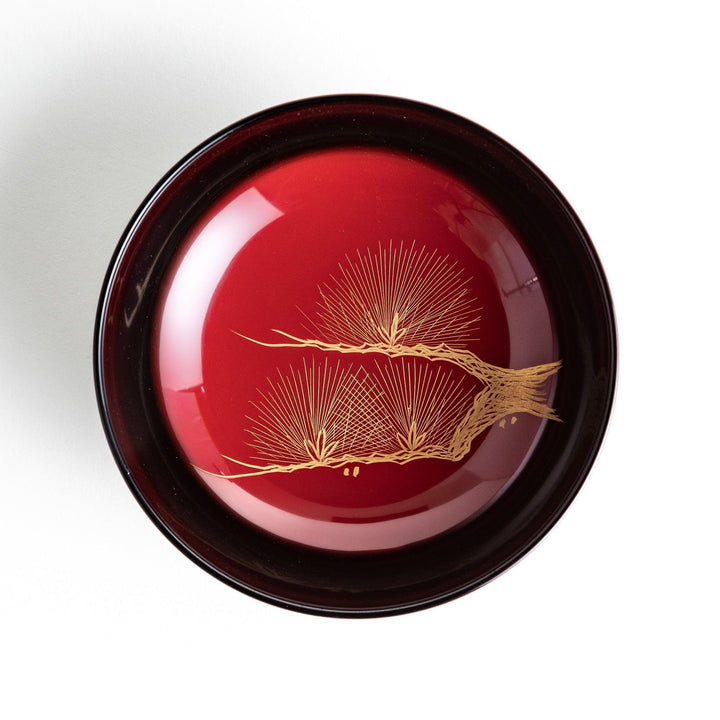Traditional black lacquer bowl with red interior, featuring a gold pine tree design on the lid.