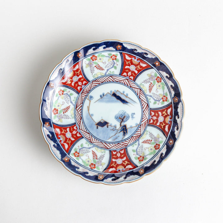 A deep porcelain bowl with an intricate Imari-style design, featuring a central landscape scene and alternating floral patterns in red, blue, and gold.