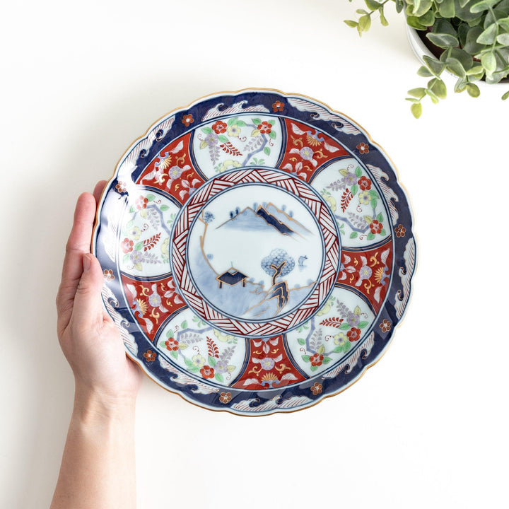 A deep porcelain bowl with an intricate Imari-style design, featuring a central landscape scene and alternating floral patterns in red, blue, and gold.