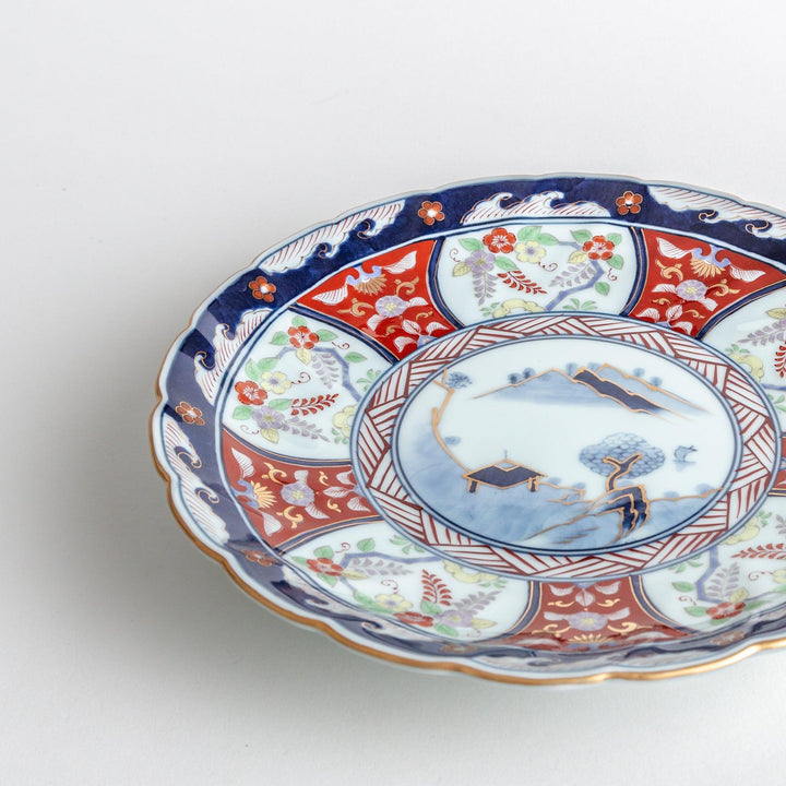 A deep porcelain bowl with an intricate Imari-style design, featuring a central landscape scene and alternating floral patterns in red, blue, and gold.