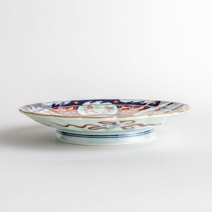 A deep porcelain bowl with an intricate Imari-style design, featuring a central landscape scene and alternating floral patterns in red, blue, and gold.