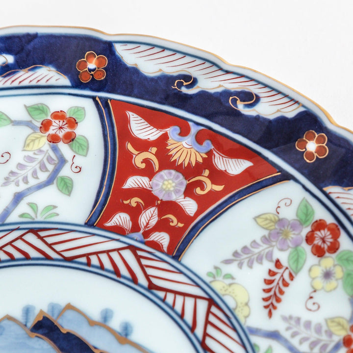 A deep porcelain bowl with an intricate Imari-style design, featuring a central landscape scene and alternating floral patterns in red, blue, and gold.
