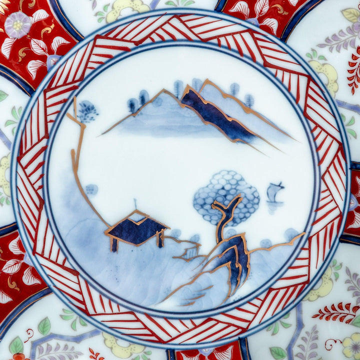A deep porcelain bowl with an intricate Imari-style design, featuring a central landscape scene and alternating floral patterns in red, blue, and gold.