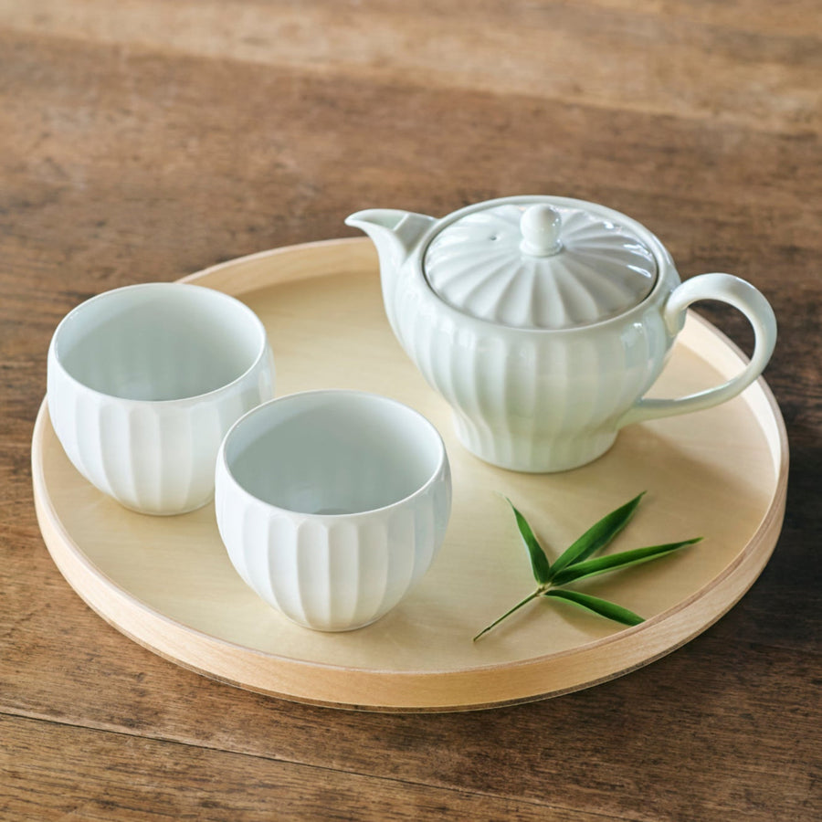 Handcrafted Petal White Tea Set featuring a teapot and two cups on a round wooden tray, accented with a green leaf on a rustic table.