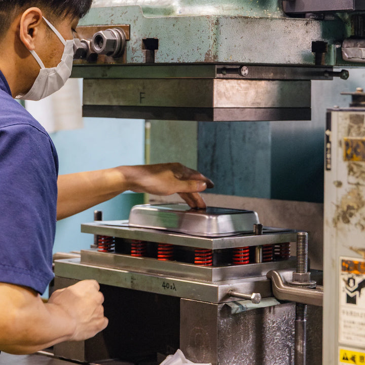 Artisan shaping stainless steel container in a press machine during careful precision manufacturing