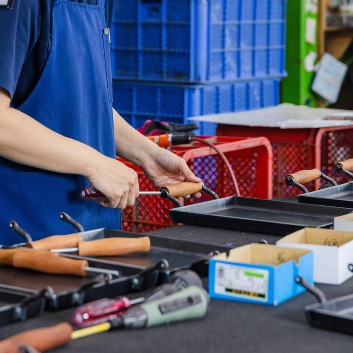 Artisan assembling wooden handles onto cookware in a detailed hand finished production process