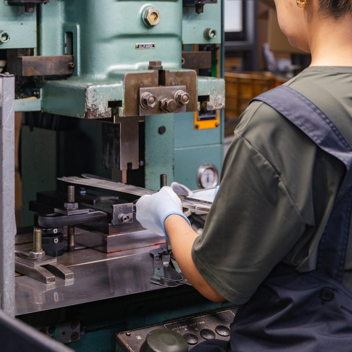 Artisan guiding stainless steel pieces into a press machine during precise cookware production