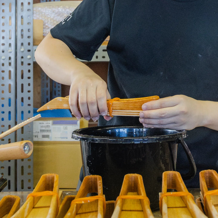 Handcrafting wooden scoops as artisan applies finish in a workshop setting