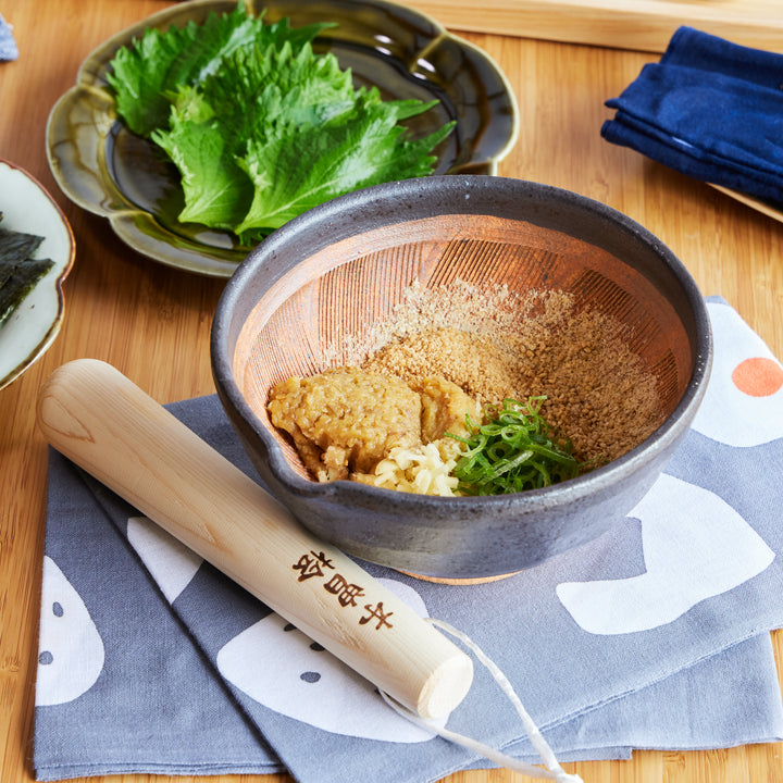 Hinoki wood pestle and ceramic mortar set shown with ground sesame and condiments, ideal for Japanese cooking.