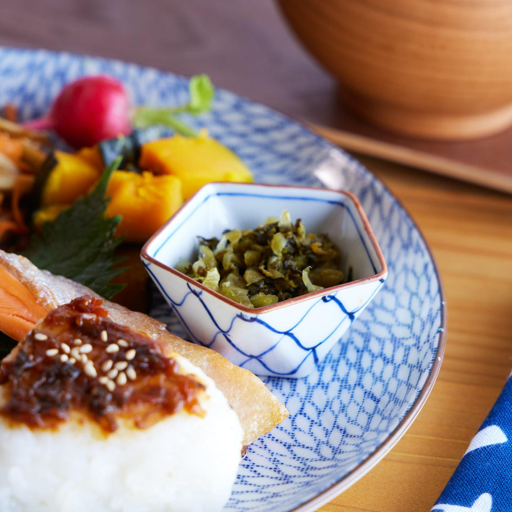 Pentagonal Japanese condiment bowl with blue mesh pattern filled with Japanese pickles, placed on a patterned plate.