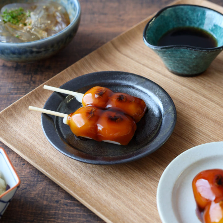 Round black dessert plate with a subtle sheen, beautifully presenting skewered mitarashi dango on a wooden tray for an elegant Japanese sweets display.