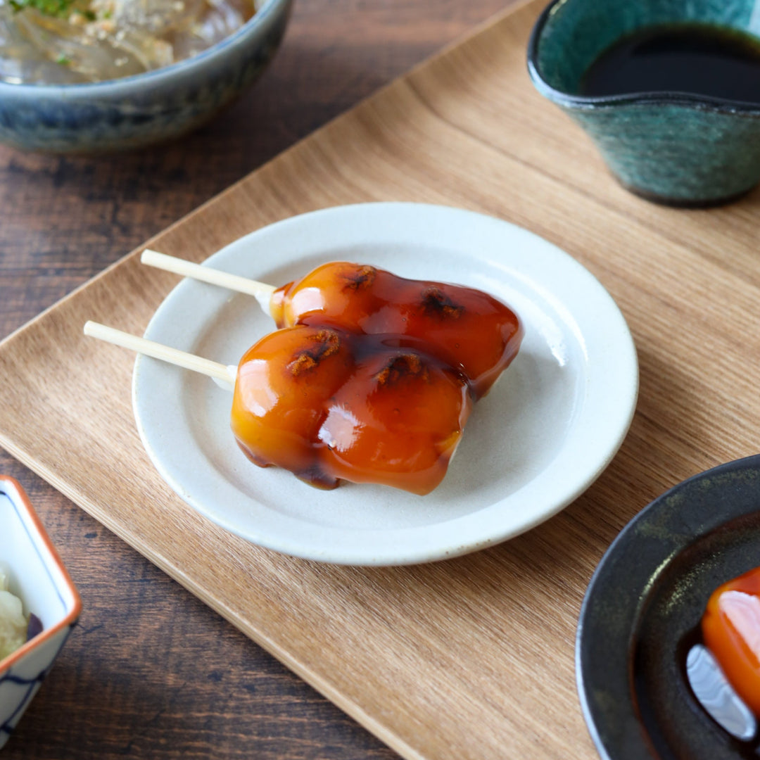 Round white dessert plate with a smooth matte finish, elegantly showcasing mitarashi dango skewers on a wooden tray for a classic Japanese sweets presentation.