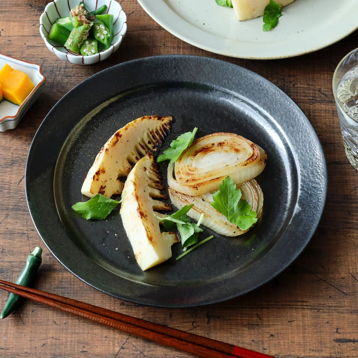 Grilled bamboo shoots and onions served on a black pottery Japanese dinner plate with a subtle metallic sheen.