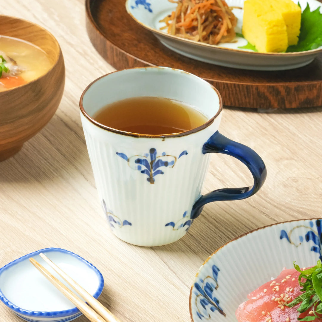 A Japanese porcelain mug with ribbed texture and blue floral leaf motifs, filled with tea and paired with a meal.