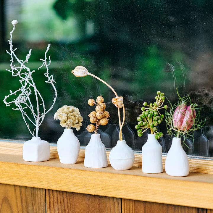 Minimalist white ceramic bud vases in varied shapes on a windowsill showcasing assorted dried flower stems for home decor.