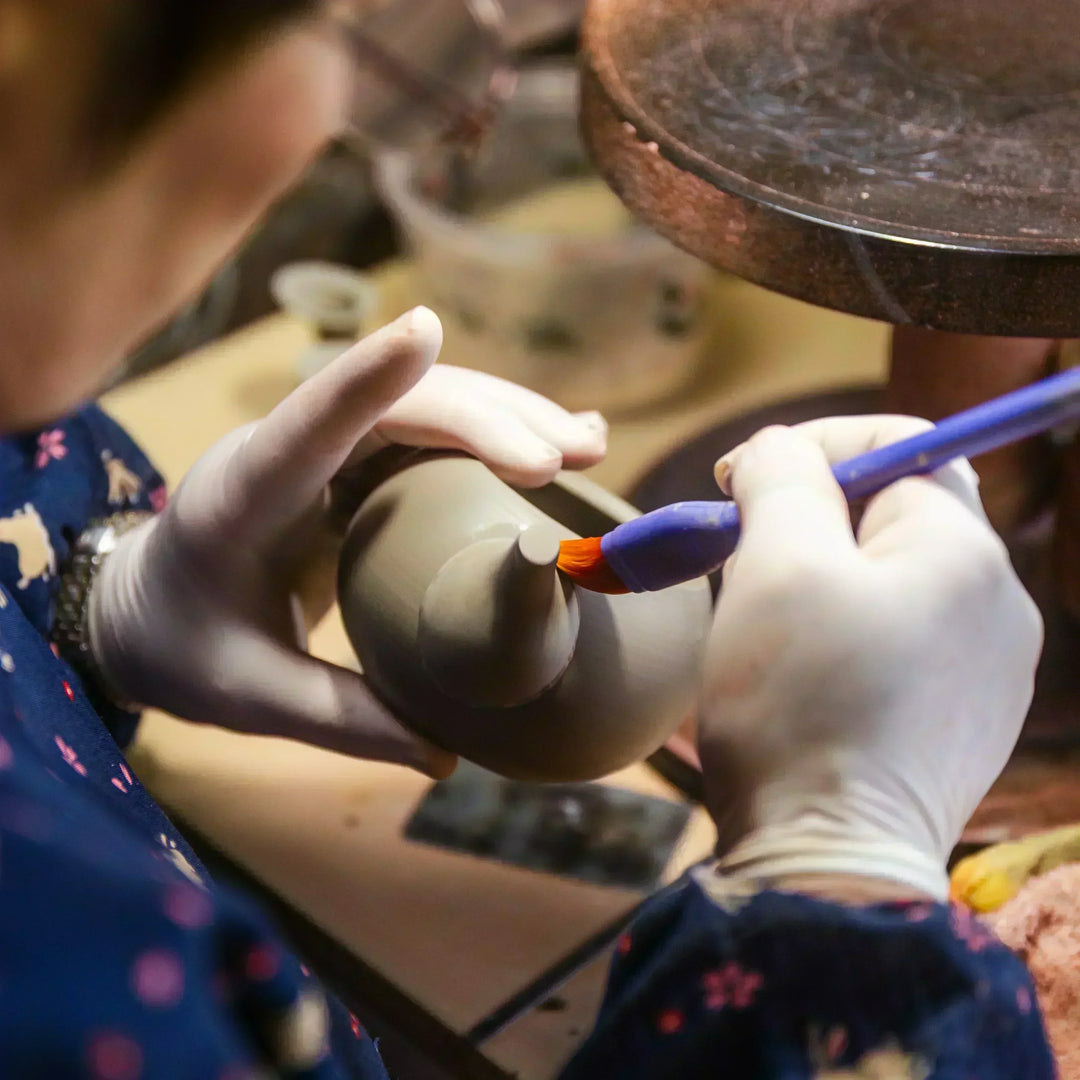 Artisan brushing the surface of a clay teapot during detailed hand finishing in a pottery workshop