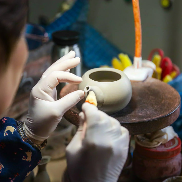 Artisan smoothing the spout opening of a clay teapot with delicate handwork in a pottery studio