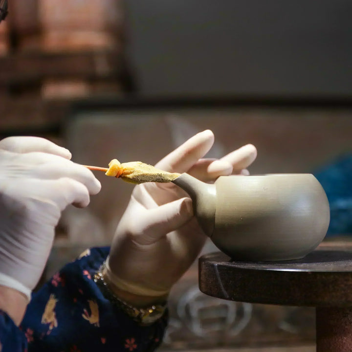 Artisan refining the spout of a clay teapot with careful hand finishing in a traditional pottery workshop