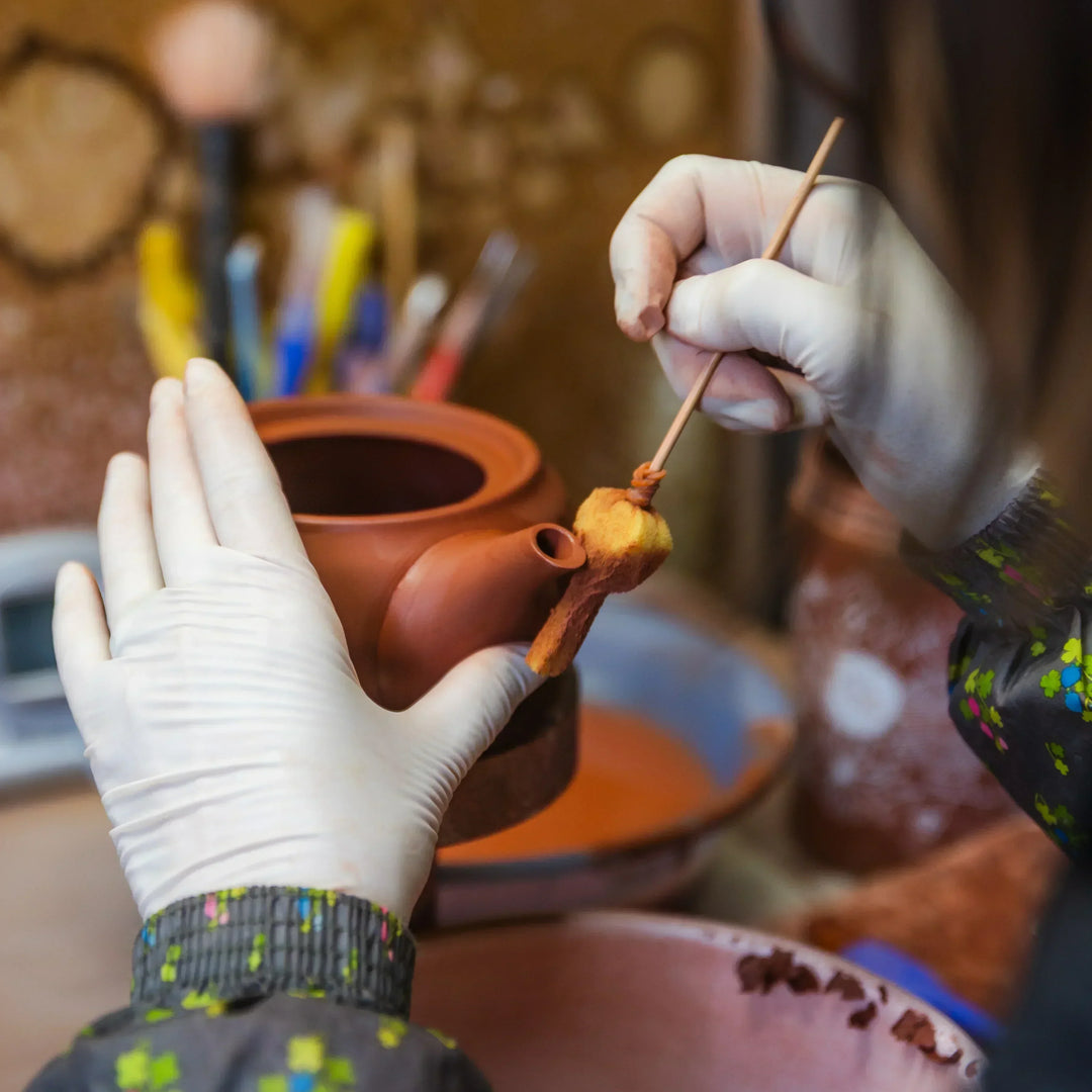 Artisan refining the spout area of a clay teapot with careful handwork in a traditional pottery studio