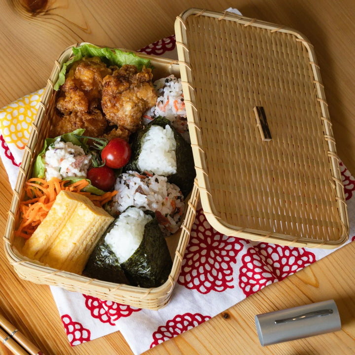 Japanese goza weave bamboo bento box filled with onigiri rice balls and karaage fried chicken on a wooden table