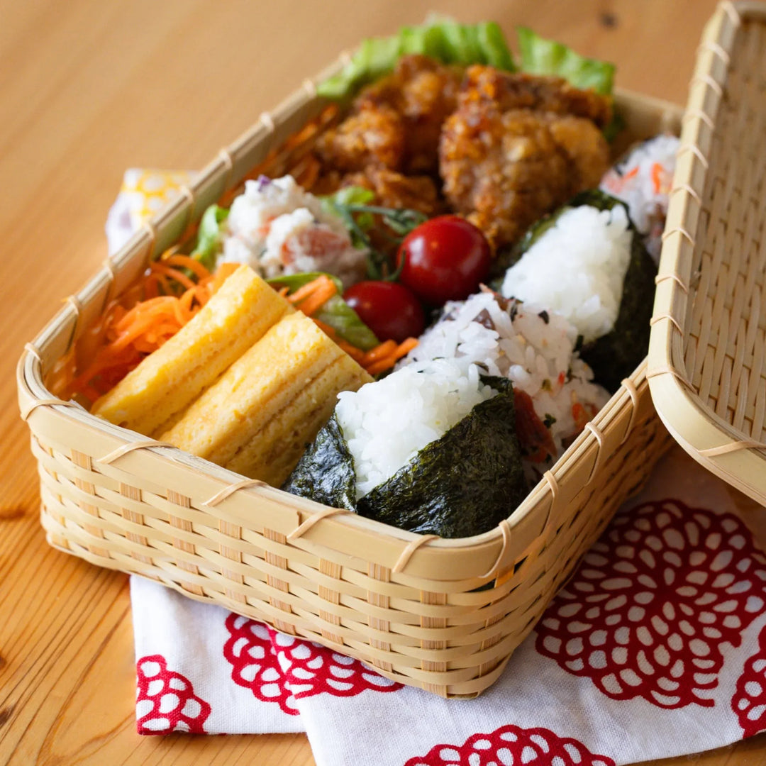 Close up of a handcrafted Japanese goza weave bamboo bento box filled with fresh onigiri and colorful side dishes