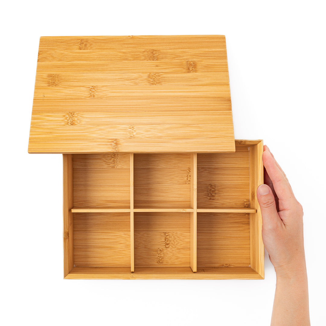 Top down view of an open bamboo bento box with a hand revealing six equal inner compartments for perfect food portioning