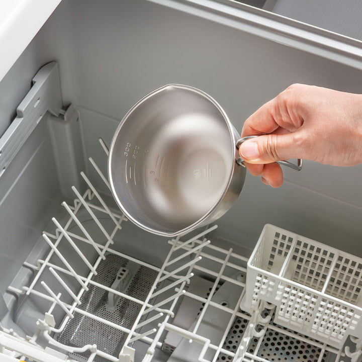 Person placing a stainless steel egg beating bowl with handle into an open dishwasher rack