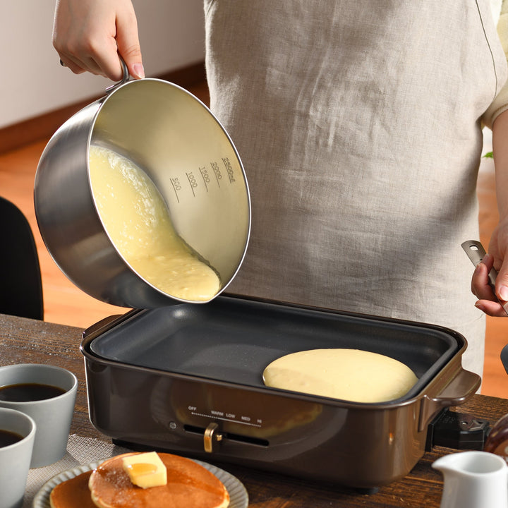 Person pouring pancake batter from an AUX Japanese Stainless Steel Mixing Bowl with Handle onto an electric griddle