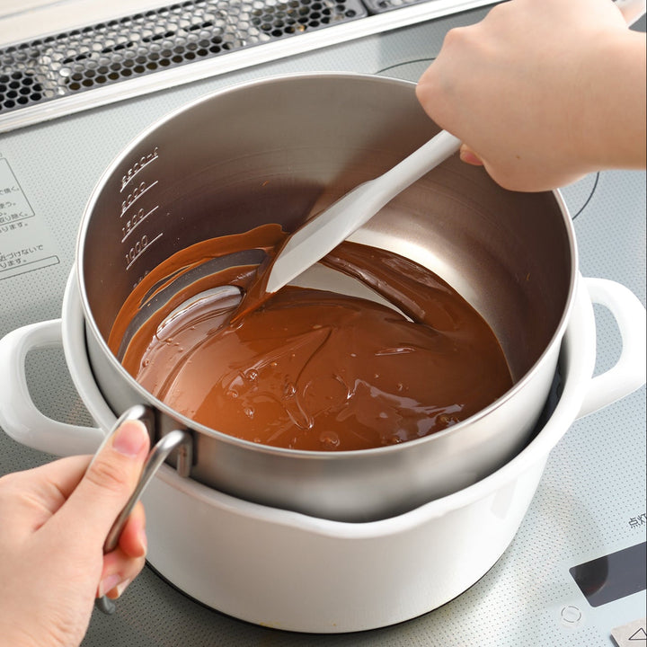 Person stirring melted chocolate inside an AUX Japanese Stainless Steel Mixing Bowl with Handle set over a hot water bath