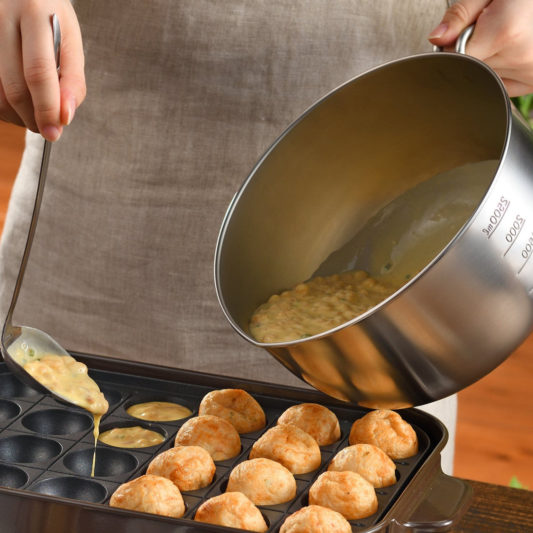 Person holding an AUX Japanese Stainless Steel Mixing Bowl with Handle while scooping batter into a takoyaki pan
