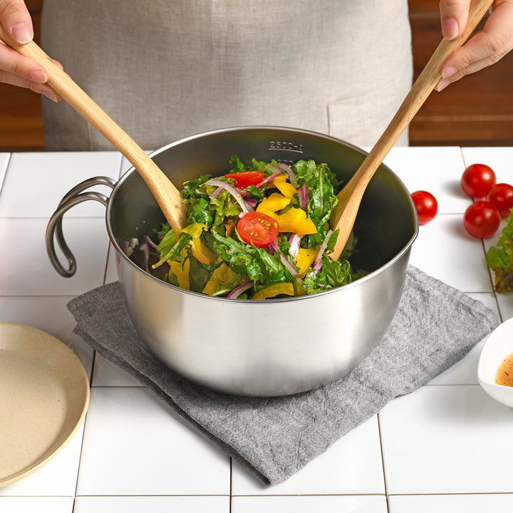 Person tossing a fresh green salad with wooden servers inside an AUX Japanese Stainless Steel Mixing Bowl with Handle