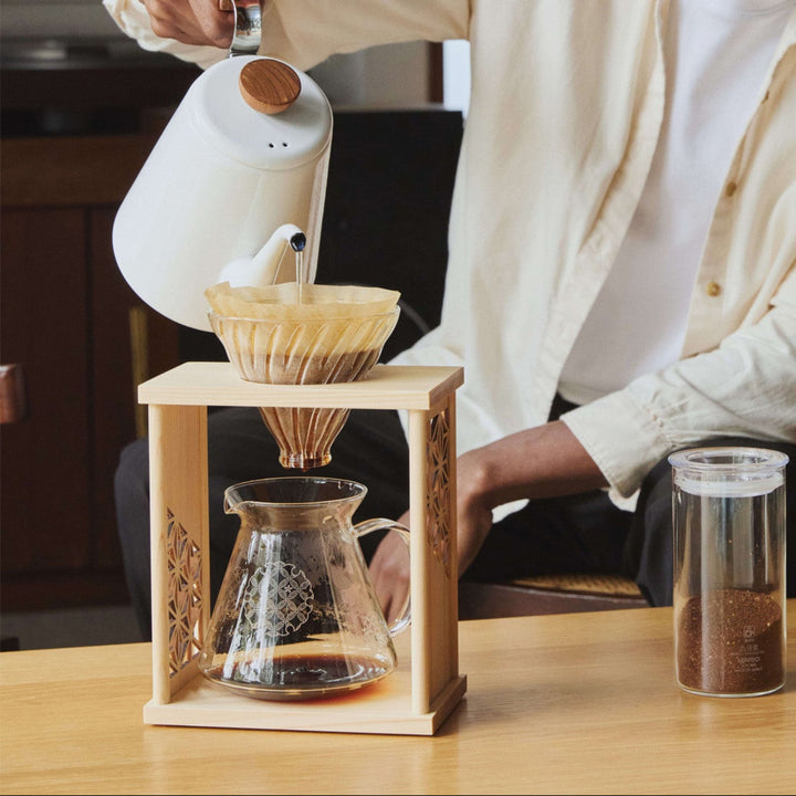 Pouring hot water from white kettle into aya asanoha wood coffee dripper set with man brewing fresh morning blend