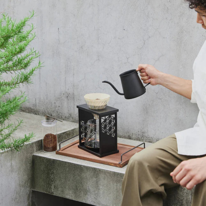 Showcasing brewed coffee inside hario aya asanoha black wood dripper set next to glass mug and small green bonsai tree