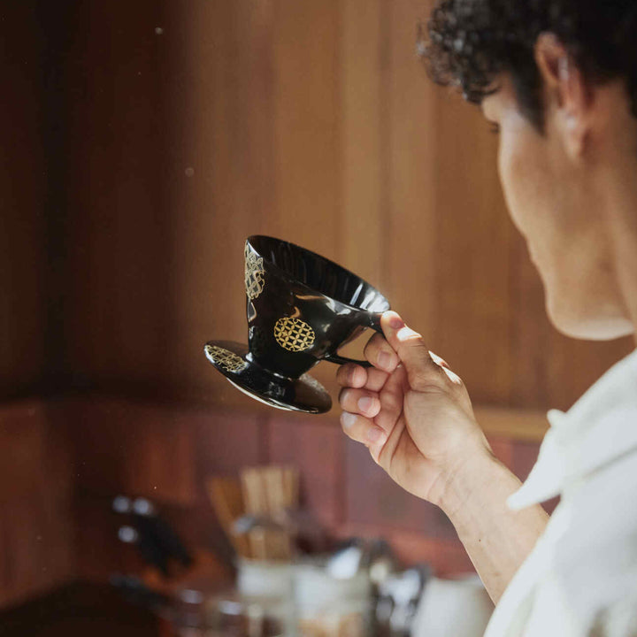 Holding black hario ceramic coffee dripper with gold pattern in wooden kitchen artisan style japanese pour over brewer