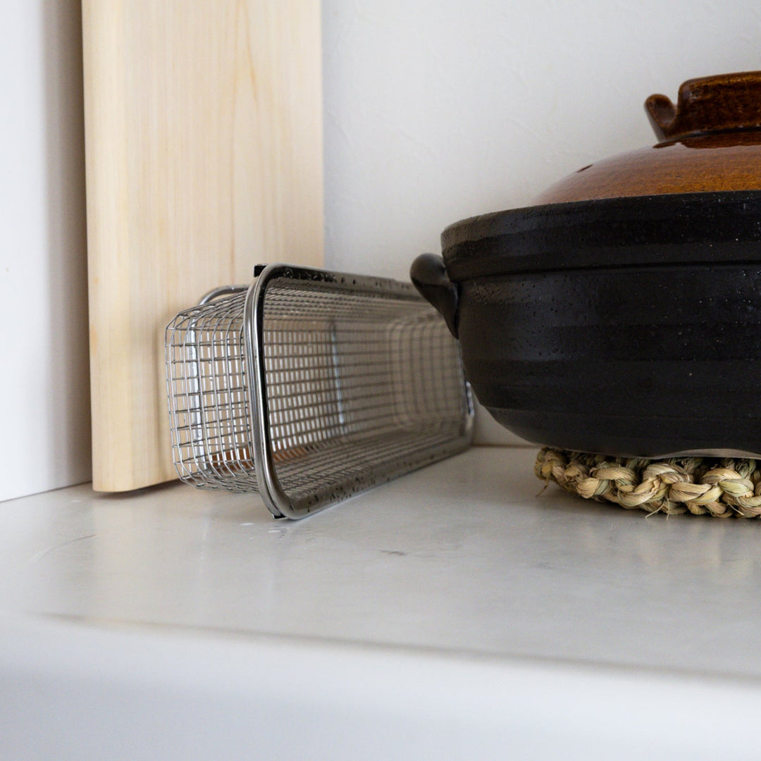 Compact adjustable stainless steel draining rack stored vertically on kitchen counter next to clay pot space saving