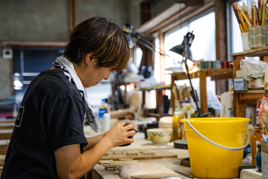 Artisan shaping ceramic pieces in a workshop filled with tools and materials, highlighting traditional handcrafted work.