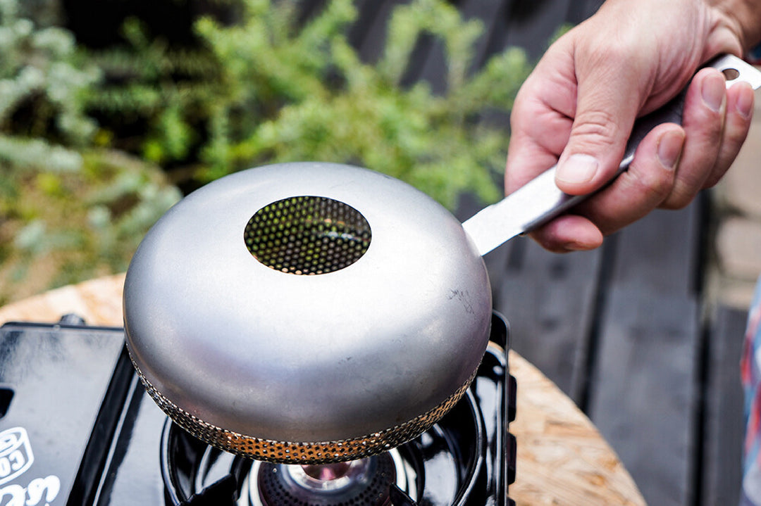 Stainless steel sesame roaster held over a portable gas stove with mesh center for even roasting
