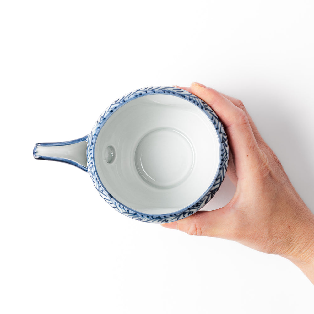 Porcelain sake pourer with spout featuring hand-painted indigo landscape and arabesque patterns in a traditional Japanese style.