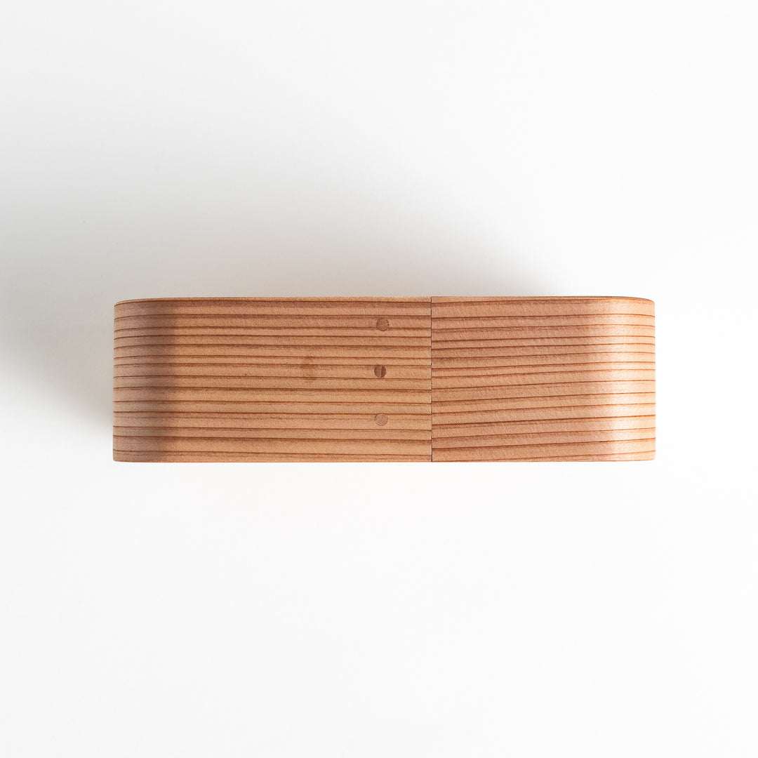 Side view of the Artisan Cedar Bento Box, showcasing its sleek, striped texture and smooth, rounded edges with visible joinery details.