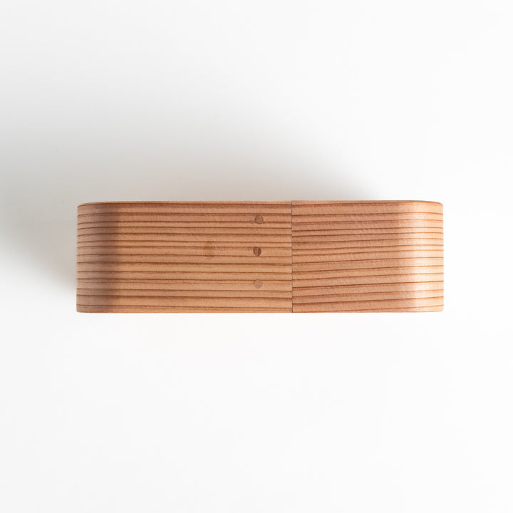 Side view of the Artisan Cedar Bento Box, showcasing its sleek, striped texture and smooth, rounded edges with visible joinery details.