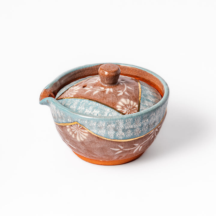 Ceramic teapot with lid featuring a turquoise crackle glaze and floral patterns in soft brown tones accented by a curved gold line.