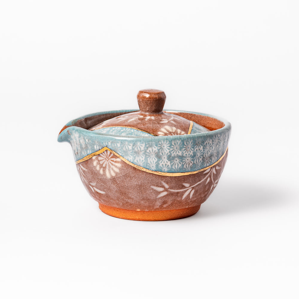 Ceramic teapot with lid featuring a turquoise crackle glaze and floral patterns in soft brown tones accented by a curved gold line.