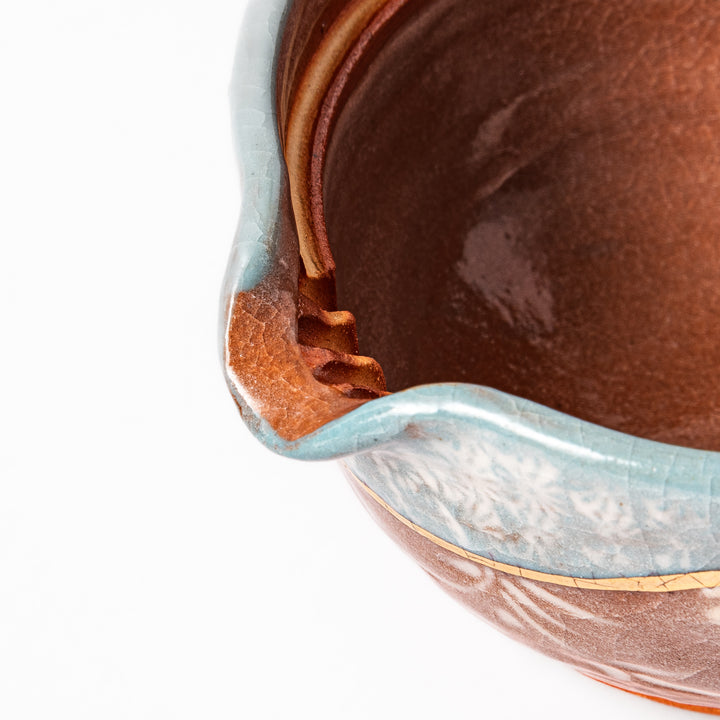 Ceramic teapot with lid featuring a turquoise crackle glaze and floral patterns in soft brown tones accented by a curved gold line.